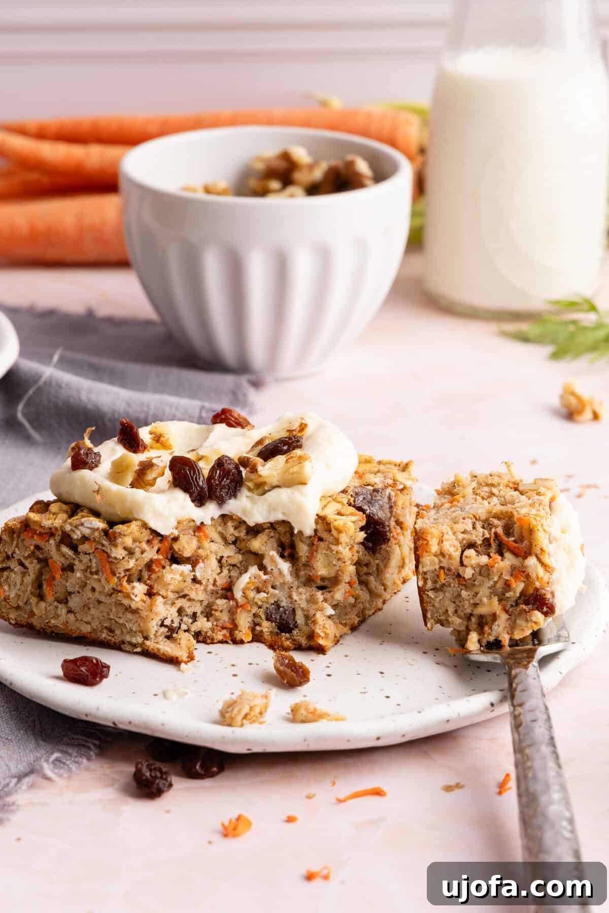 Protein-Packed Carrot Cake Oatmeal Bake 10 Close-up of carrot cake baked oats slice topped with protein cream cheese frosting, walnuts, and raisins.