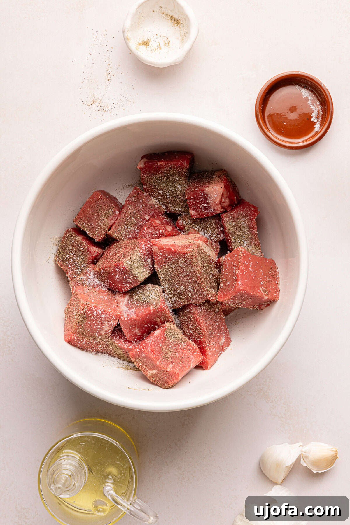 raw steak bites in a bowl with salt and pepper surrounded by ingredients