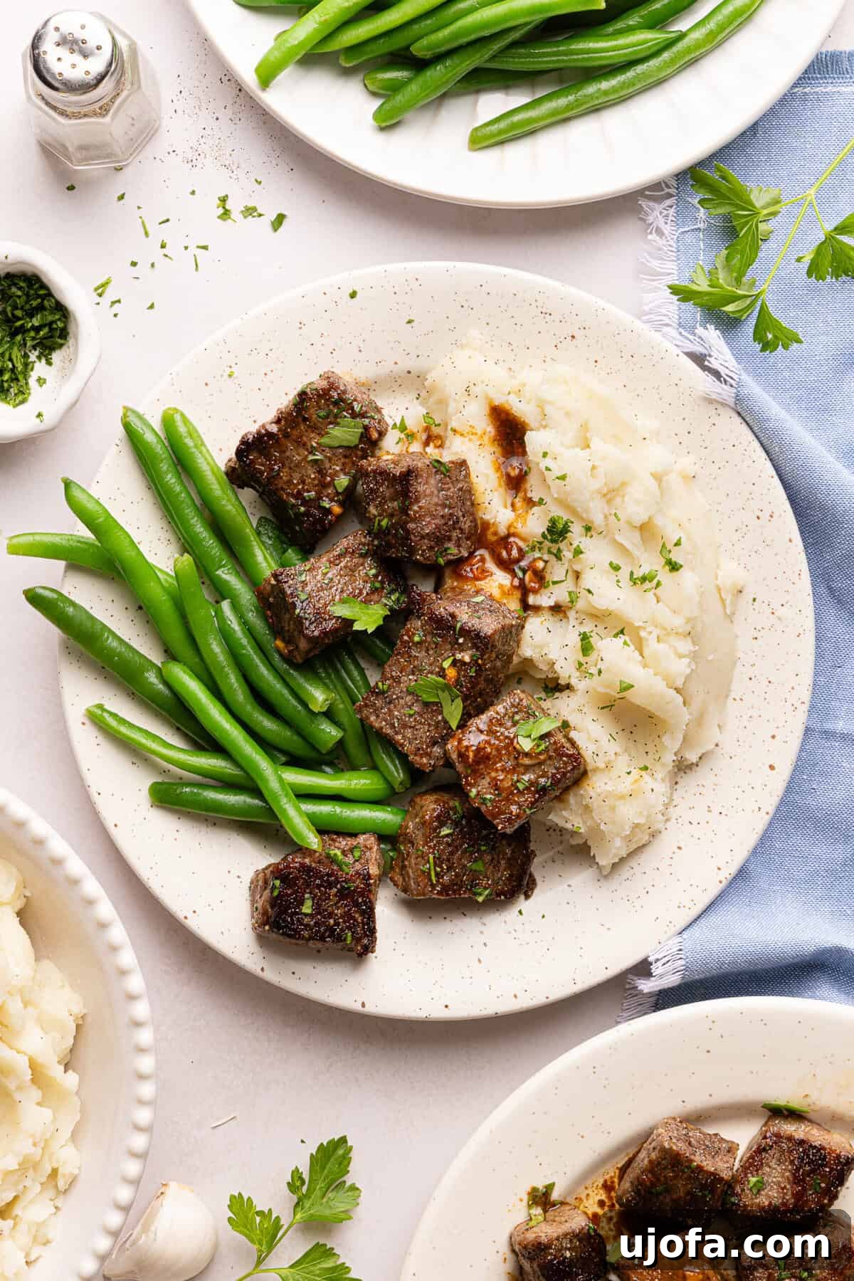 steak bites, mashed potatoes, and green beans on a plate with a blue napkin