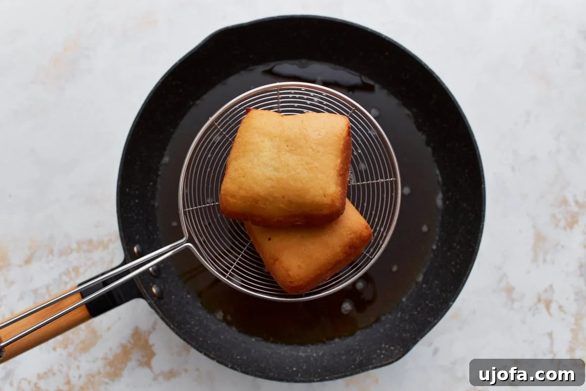 Pillowy Gluten-Free Beignets 11 Fried gluten-free beignets lifted from hot oil with a wire strainer, golden and crisp.