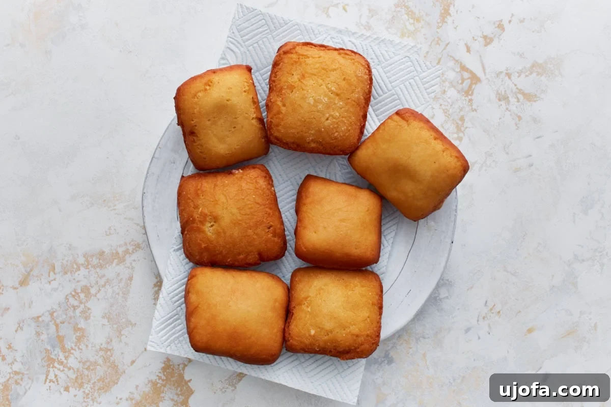 Pillowy Gluten-Free Beignets 12 Freshly fried beignets resting on a paper towel–lined plate to drain excess oil.