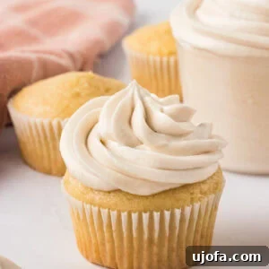 Vanilla cupcake topped with a tall swirl of creamy dairy-free buttercream frosting, with unfrosted cupcakes in the background.