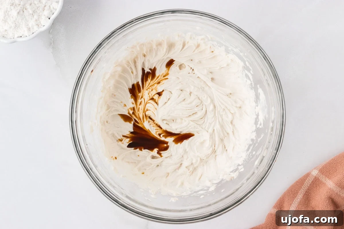 Glass mixing bowl filled with whipped dairy-free butter, with vanilla extract added on top before mixing.