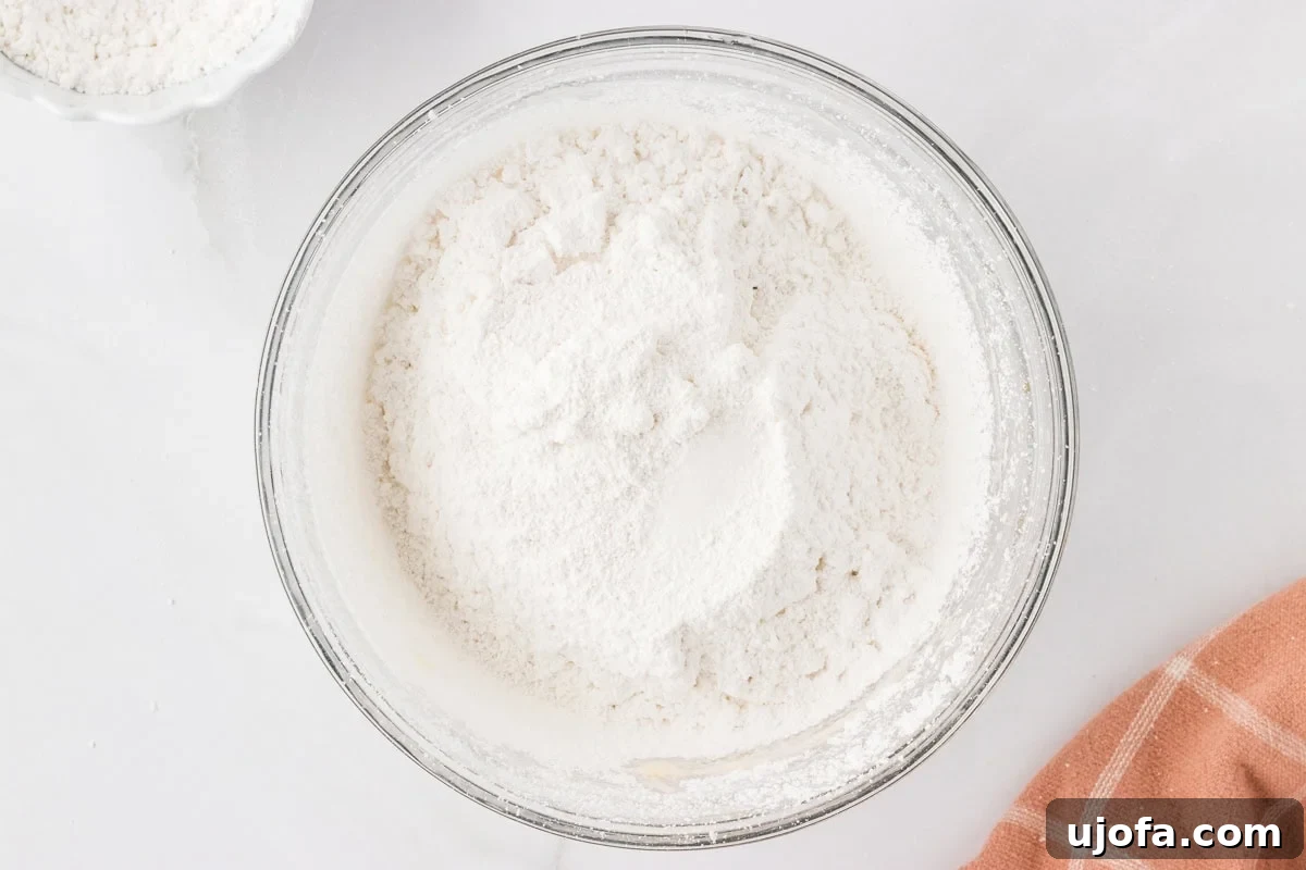 Sifted powdered sugar sitting on top of whipped dairy-free butter in a mixing bowl.