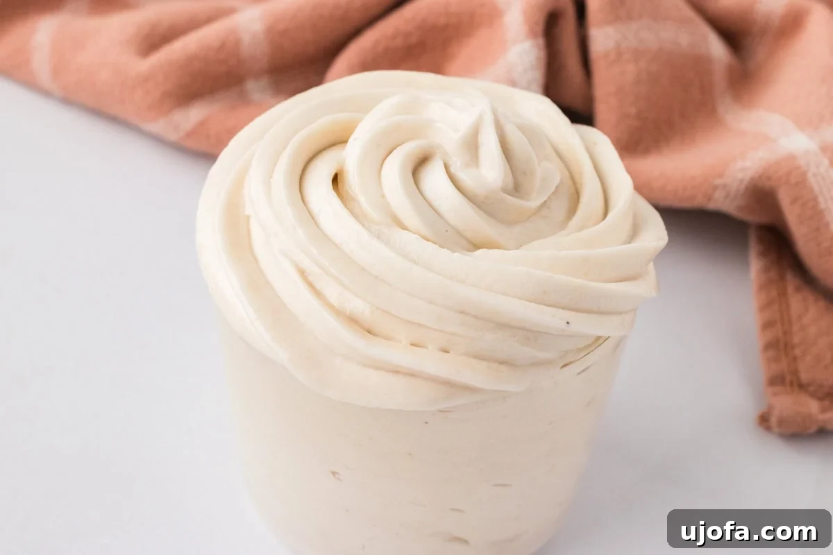 Piping bag-style swirl of dairy-free buttercream frosting in a small container with a soft cloth in the background.