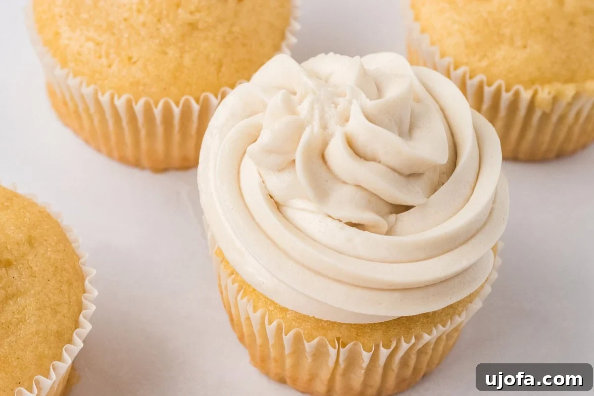 Vanilla cupcake topped with a swirl of dairy-free buttercream frosting surrounded by unfrosted cupcakes.