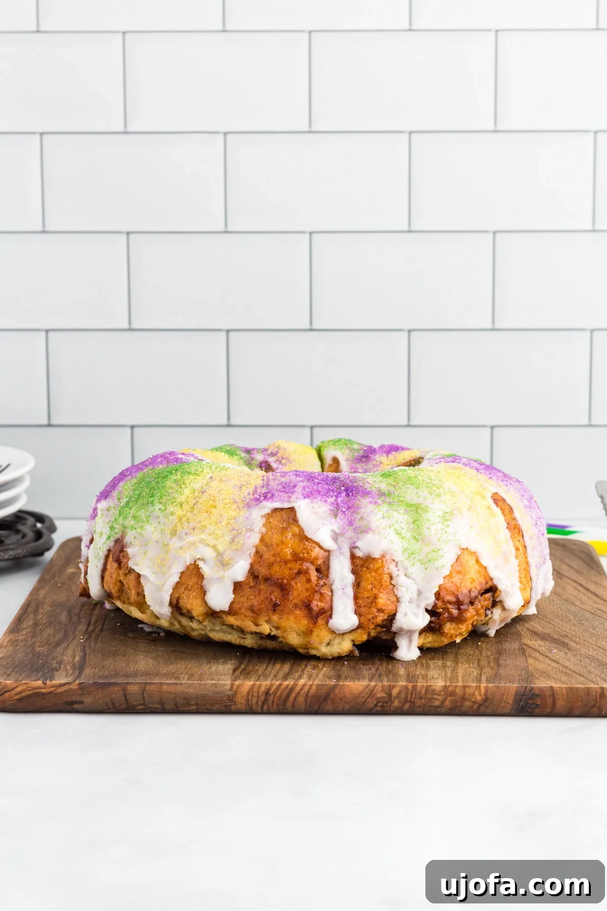 Mardi Gras Magic: Gluten-Free King Cake 2 Gluten free king cake topped with white vanilla glaze and purple, green, and gold sanding sugar on a wooden board.