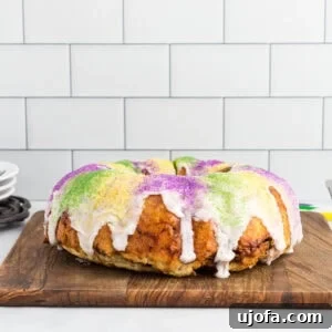 Gluten free king cake topped with white vanilla glaze and purple, green, and gold sanding sugar on a wooden board.