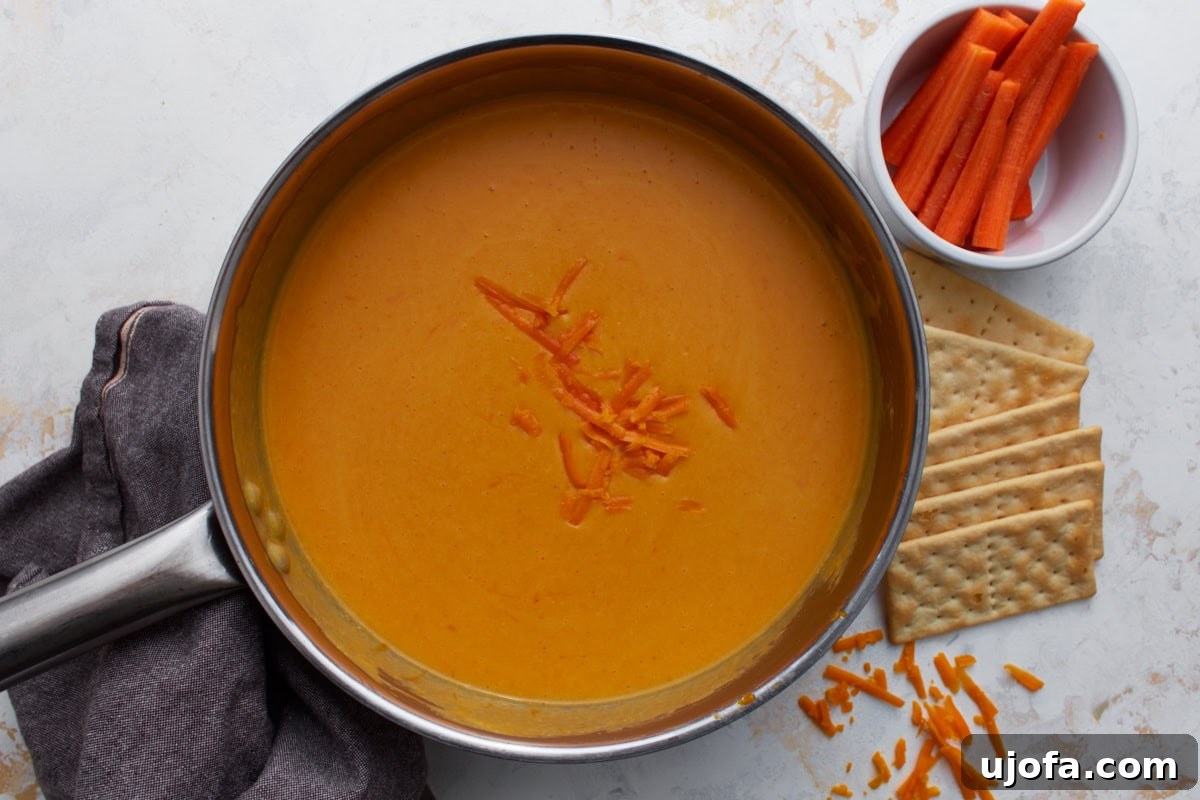 finished gluten-free beer cheese sauce in a saucepan with carrots and crackers nearby for dipping