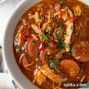 Bowl of gluten free chicken and sausage gumbo garnished with fresh parsley showing rich broth, shredded chicken, and sliced andouille.