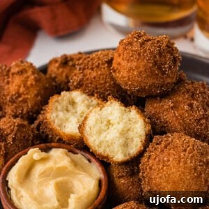 Gluten free hush puppies piled on a plate with one split open showing the soft center, served with honey butter.