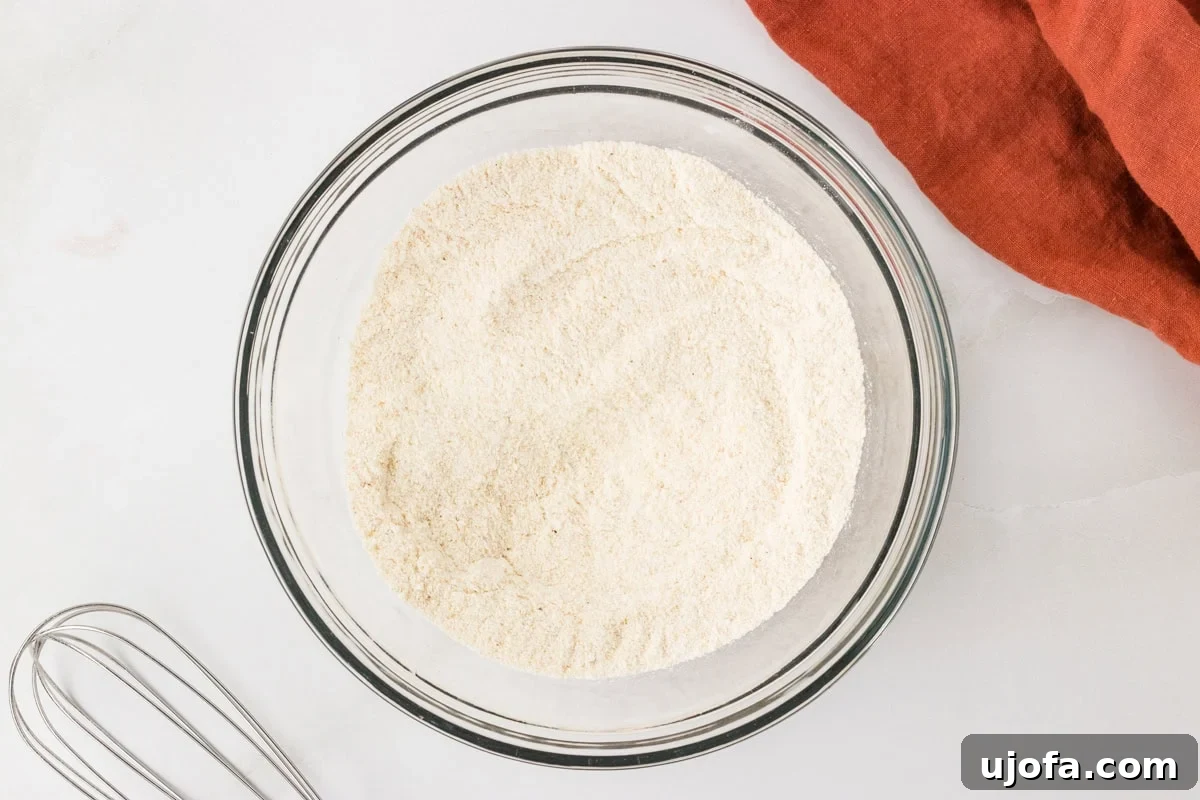 Mixed dry ingredients for gluten free hush puppies in a glass bowl with a whisk nearby.