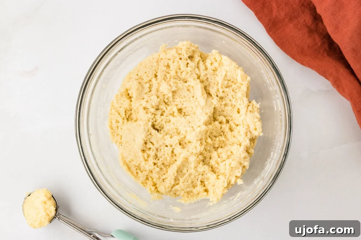 Thick gluten free hush puppy batter in a bowl with a cookie scoop showing the correct consistency.