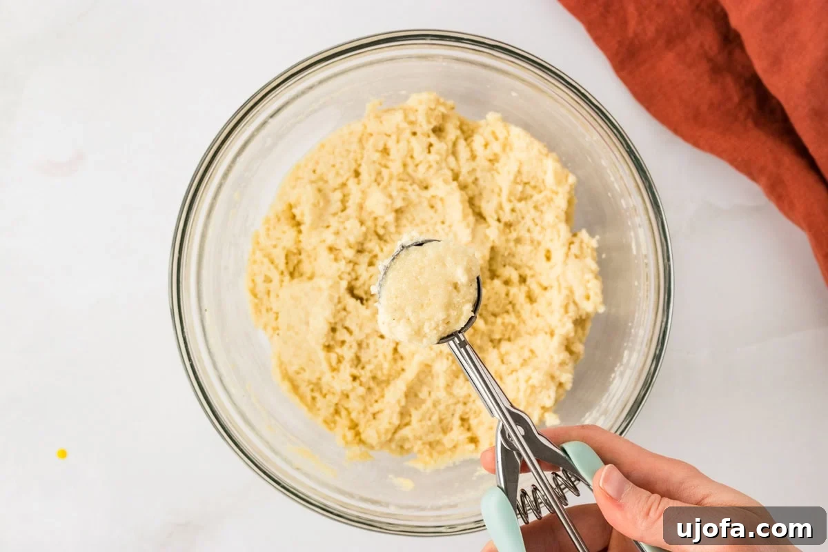Cookie scoop portioning gluten free hush puppy batter from a mixing bowl.