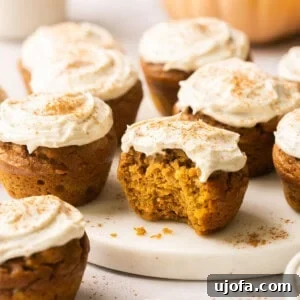 pumpkin muffins topped with cream cheese frosting and one has a bite taken out of it