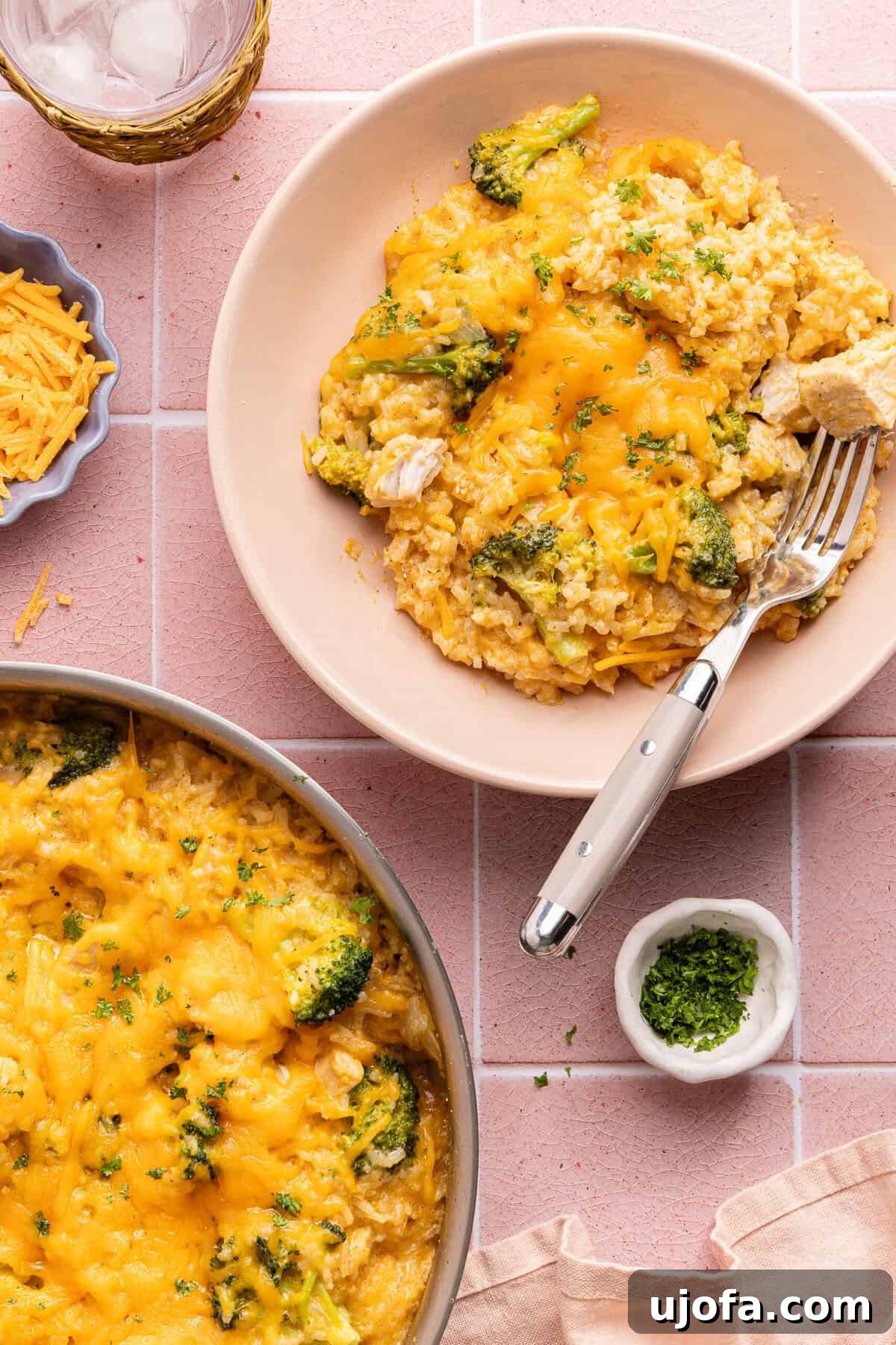 Ultimate Chicken Broccoli Rice Bake 2 A hearty bowl of cheesy chicken broccoli rice casserole with a fork, ready to be enjoyed, next to a full pan.