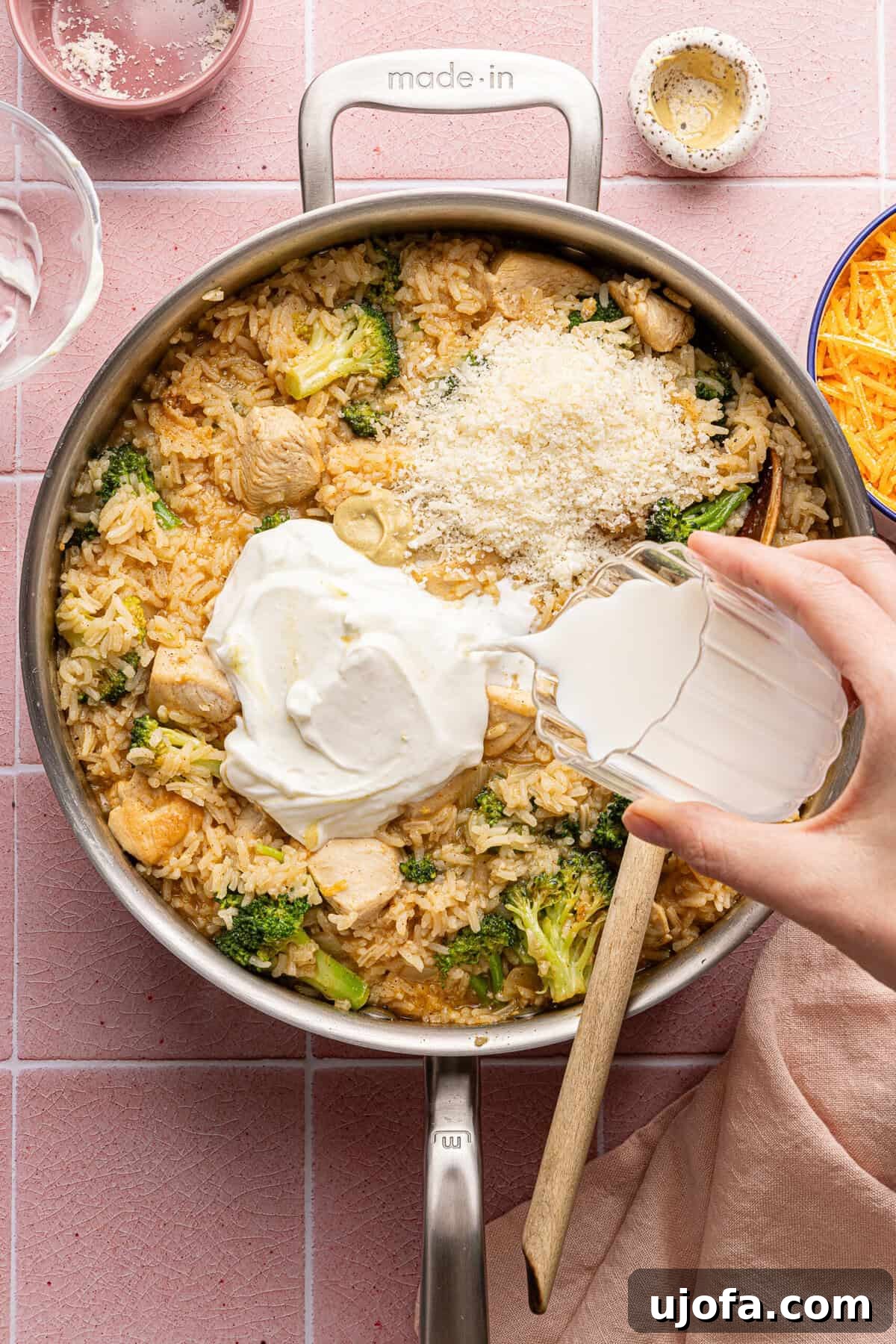 Ultimate Chicken Broccoli Rice Bake 8 Milk and Greek yogurt being stirred into a creamy chicken and rice casserole in a pan.