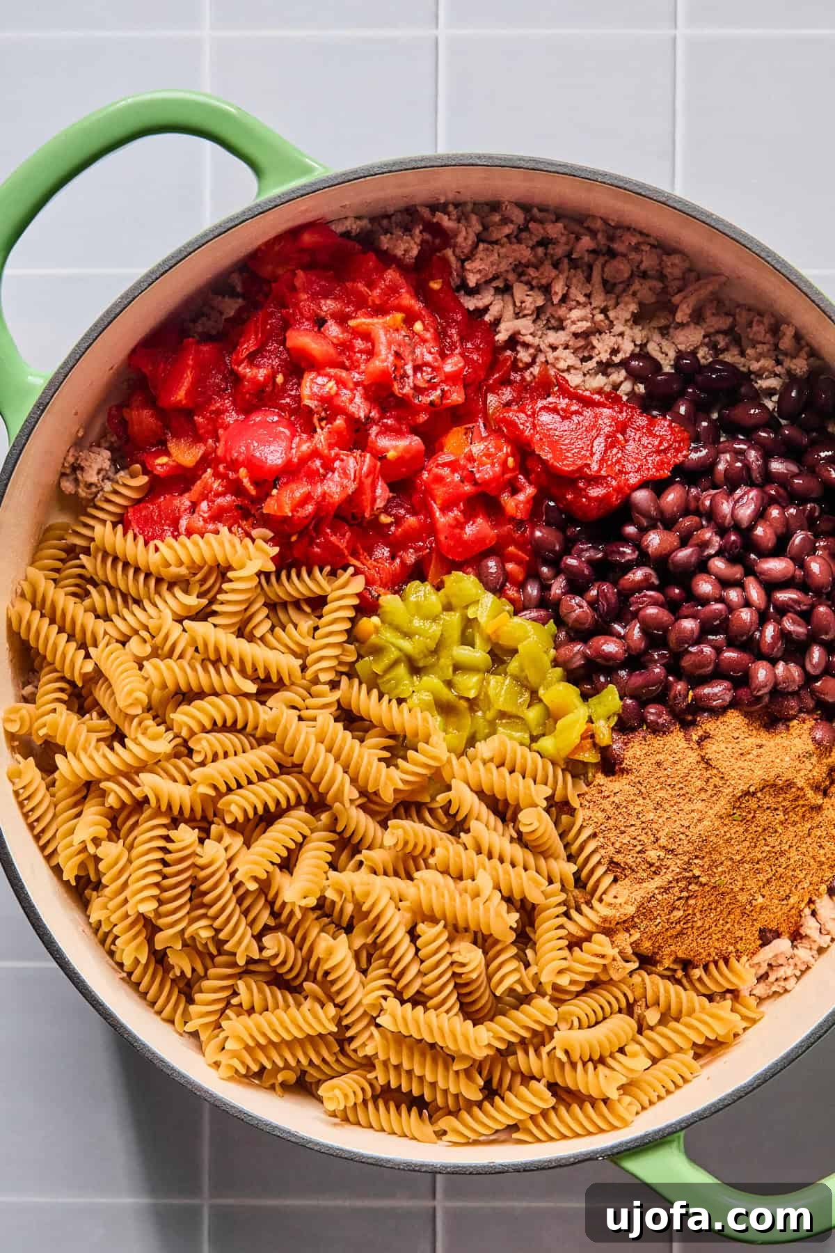 Taco seasoning, tomato paste, diced tomatoes, green chiles, black beans, and gluten-free pasta added to the skillet with browned turkey.
