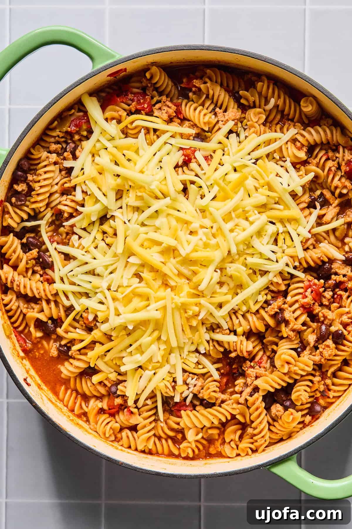 Shredded cheese being stirred into one pot taco pasta until melted and creamy, creating a luscious sauce.