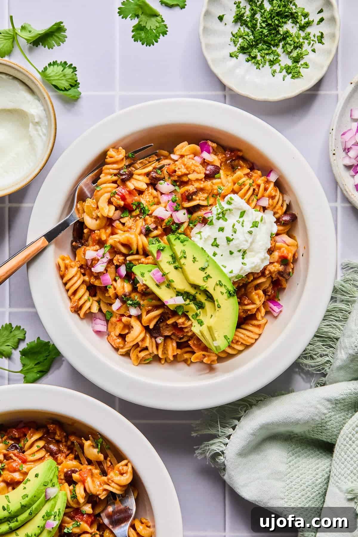Bowl of one pot taco pasta garnished with sour cream, avocado, and cilantro, with a fork ready to enjoy.