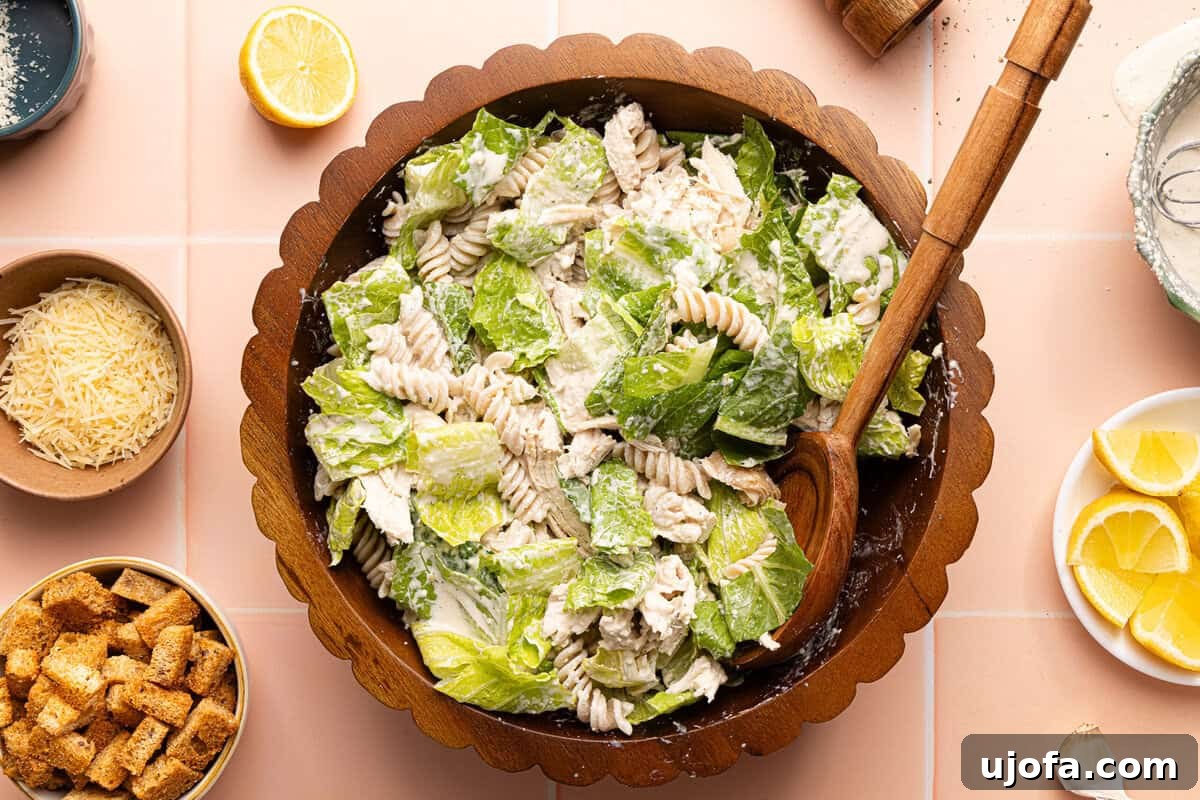 Effortless Gluten-Free Chicken Caesar Pasta Salad 7 chicken caesar pasta salad tossed together in a wooden bowl with a wooden spoon