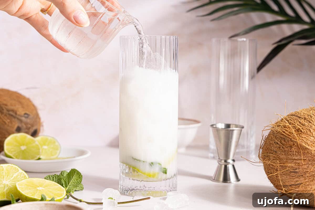 Dreamy Coconut Mojito 8 Club soda being gently poured into the glass, topping off the coconut mojito, creating a frothy layer.