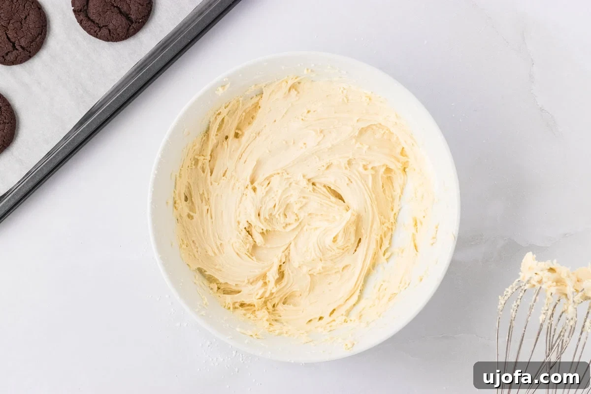 A white bowl filled with fluffy vanilla marshmallow filling, next to baked cookies and a whisk.