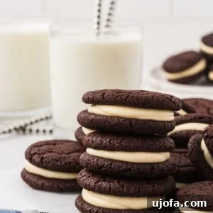 Gluten free chocolate sandwich cookies stacked on a wire rack, filled with vanilla marshmallow cream, with glasses of milk and striped straws in the background.