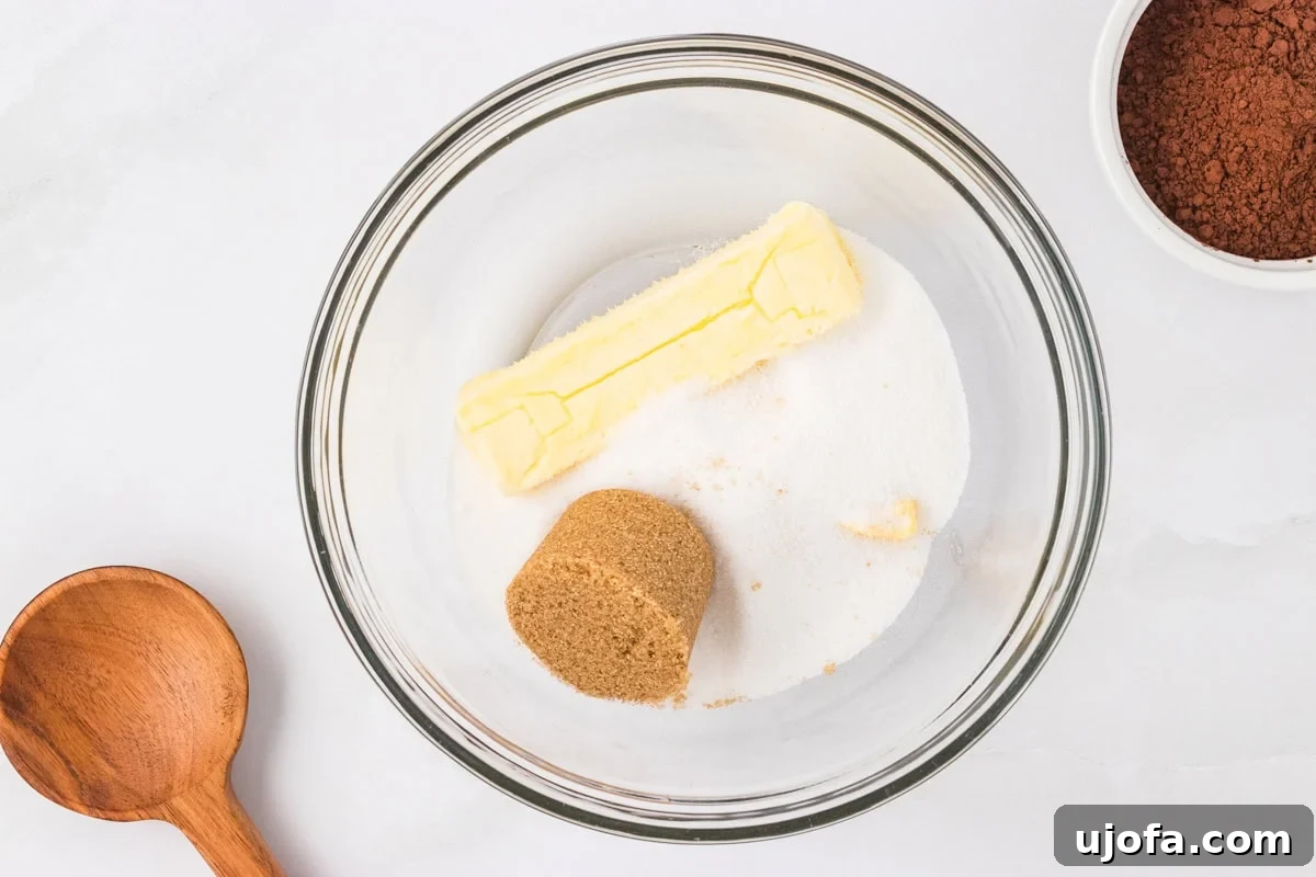 A glass mixing bowl with a stick of butter, granulated sugar, and packed brown sugar, ready to be creamed for cookie dough.