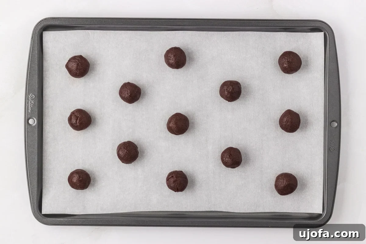 Portioned chocolate cookie dough balls evenly spaced on a parchment-lined baking sheet before baking.