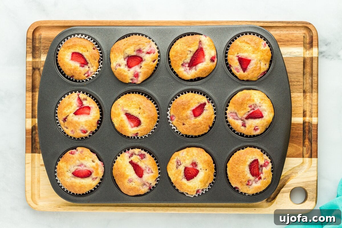 Freshly baked gluten-free strawberry muffins cooling in the muffin tin, with golden brown tops and visible strawberry pieces, indicating they are perfectly cooked.