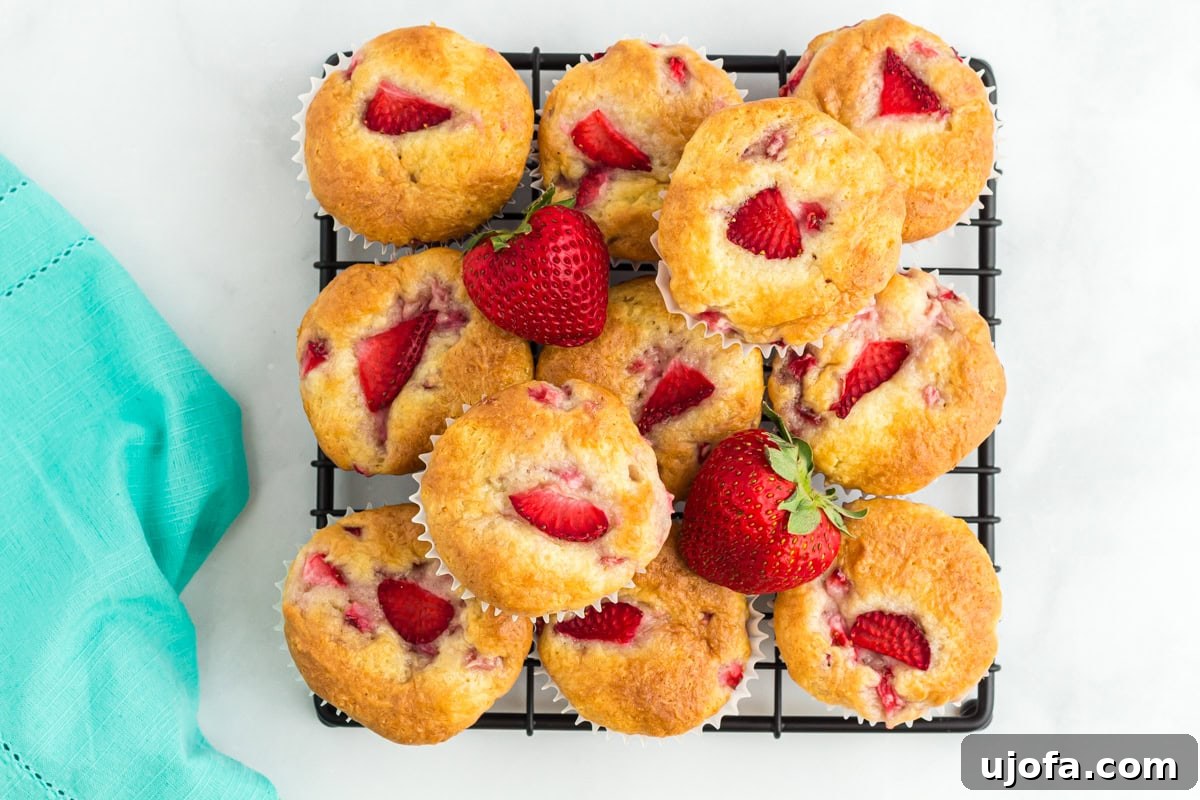 An overhead view of a delicious pile of golden gluten-free strawberry muffins arranged on a black wire cooling rack, beautifully garnished with fresh whole strawberries, highlighting their rustic charm.
