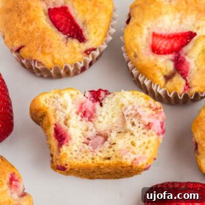 Gluten-free strawberry muffins with golden tops, one muffin cut in half to show the moist, fluffy crumb and chunks of fresh strawberries inside.