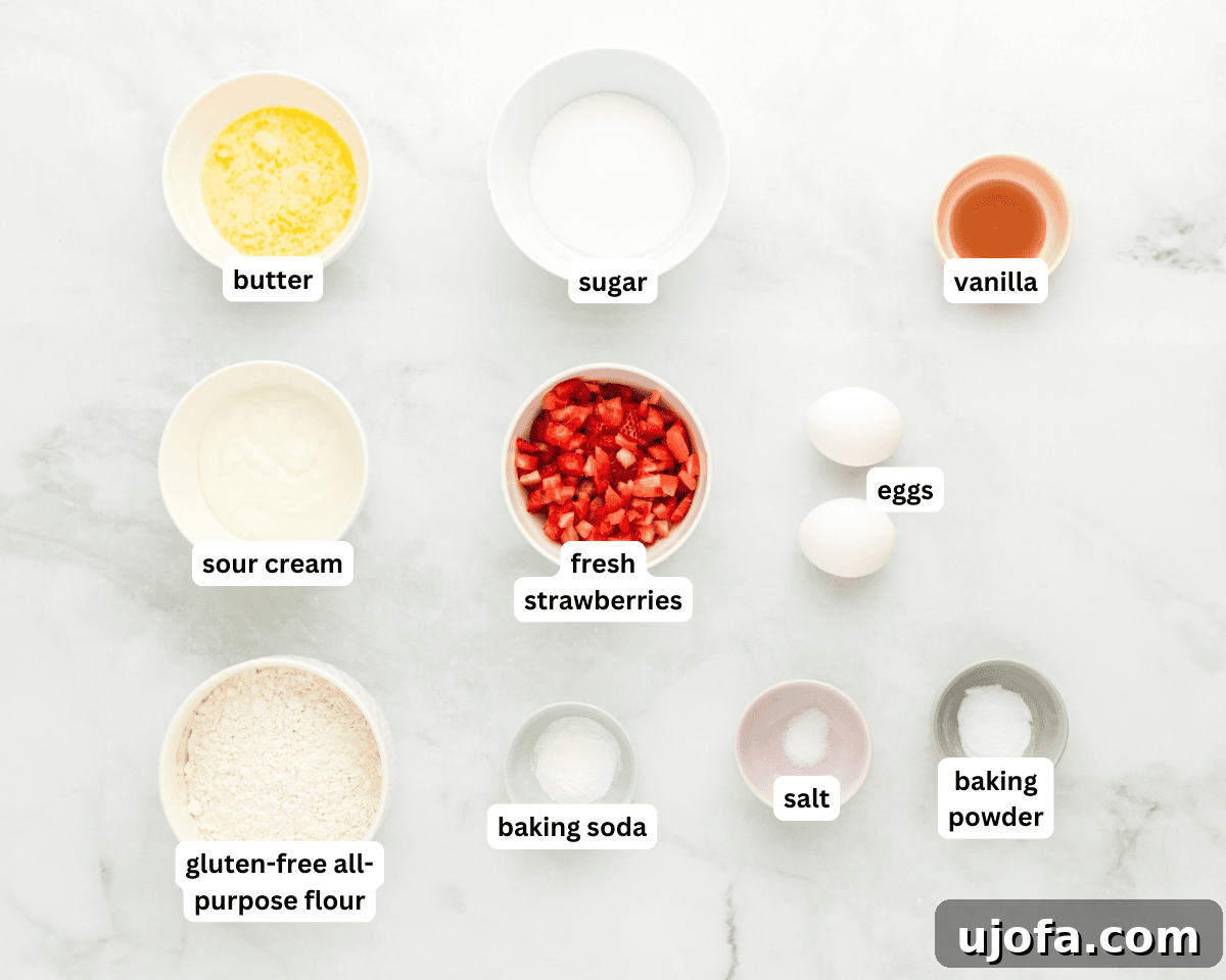 A collection of ingredients laid out on a clean surface, including bowls of gluten-free flour, fresh strawberries, eggs, butter, and other baking essentials, ready to be combined.