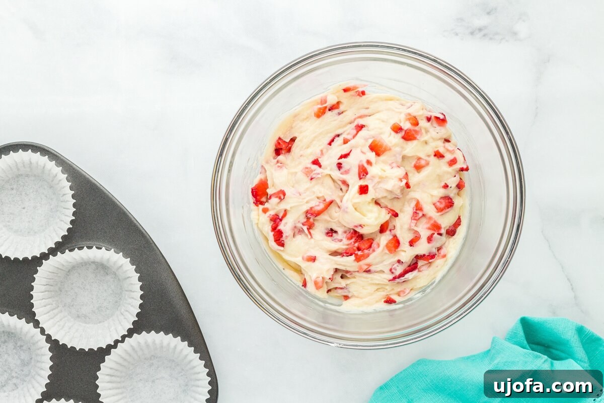 Strawberry muffin batter fully mixed in a large glass bowl, showcasing the even distribution of chopped strawberries throughout the thick, creamy mixture.