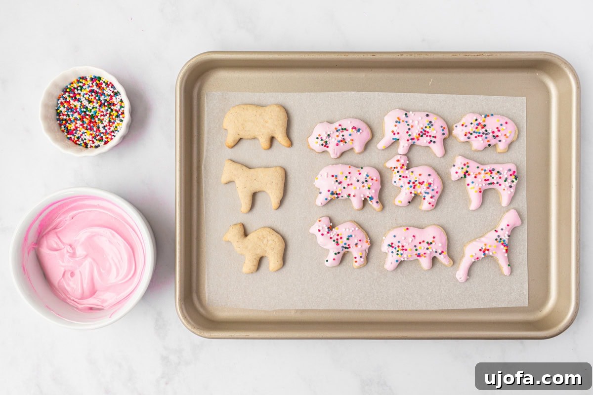 A baking sheet featuring both undecorated gluten-free animal crackers and some coated in vibrant pink candy with colorful rainbow sprinkles, ready for serving.
