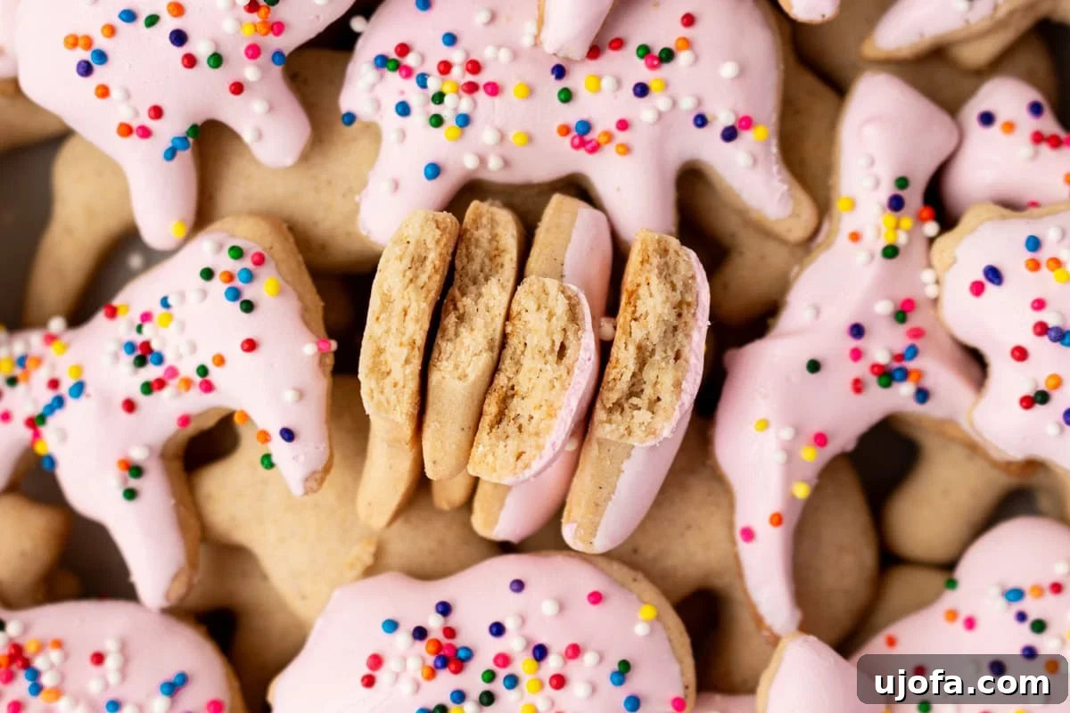 A close-up shot of several pink candy-coated gluten-free animal crackers with rainbow sprinkles, with one cracker broken in half to showcase its crisp, tender interior texture.