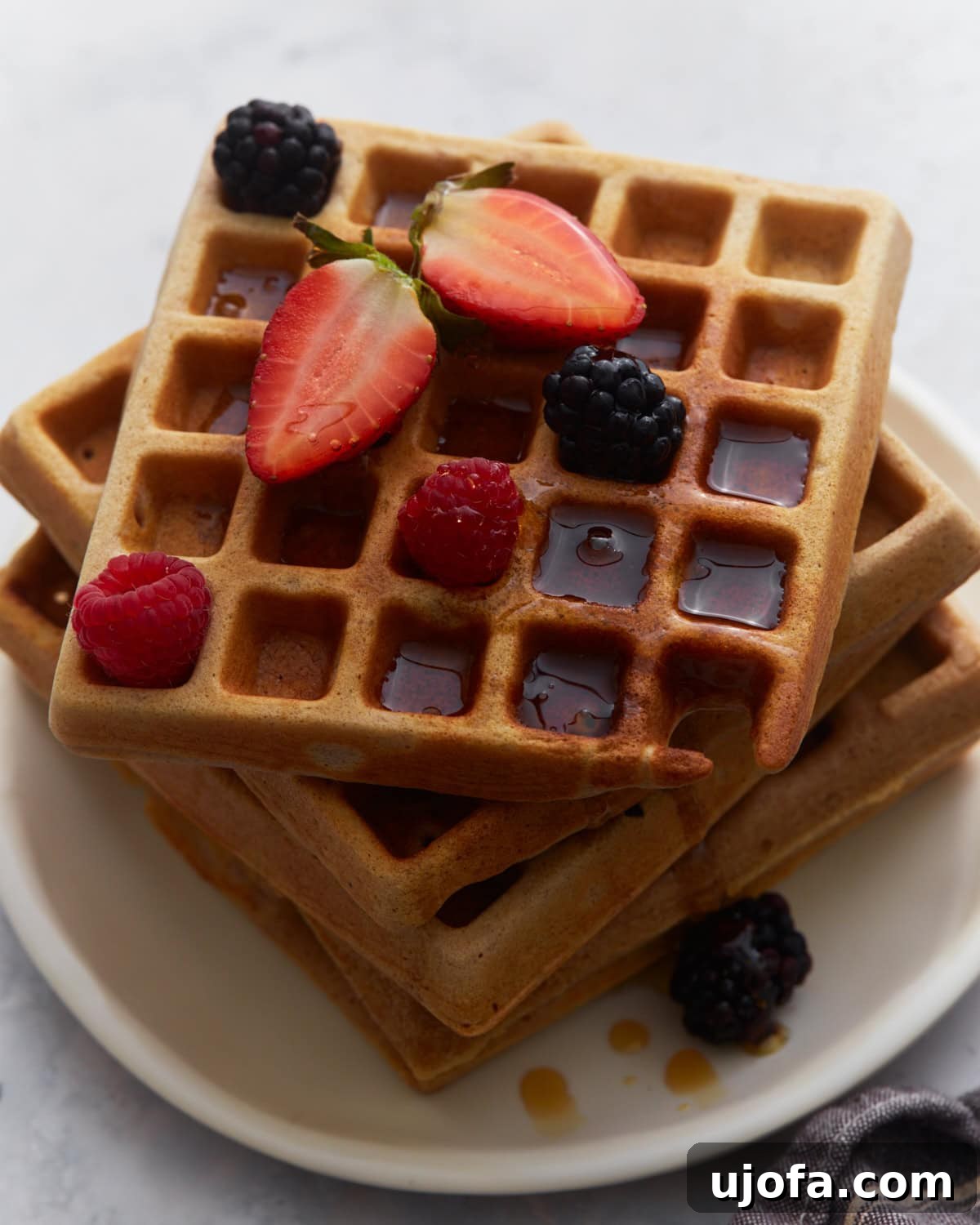 Hearty Buckwheat Waffles 2 Stacked buckwheat waffles topped with vibrant strawberries, raspberries, blackberries, and a generous drizzle of maple syrup on a pristine white plate, inviting a delicious gluten-free breakfast experience.