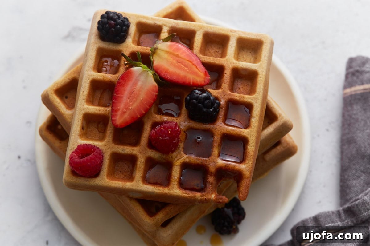 Hearty Buckwheat Waffles 9 Delicious buckwheat waffles neatly stacked on a white plate, generously topped with fresh mixed berries and a delicate drizzle of maple syrup, inviting a delightful breakfast.