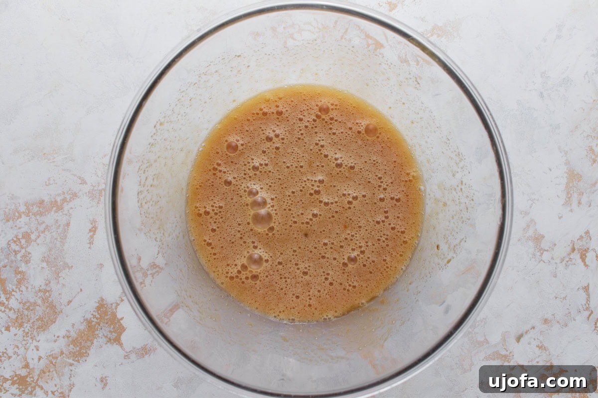 Eggs, oil, sugars, and vanilla whisked together in a glass mixing bowl until smooth and slightly frothy.
