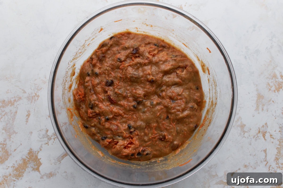 Thick carrot cake batter with shredded carrots and raisins fully incorporated in a glass bowl.