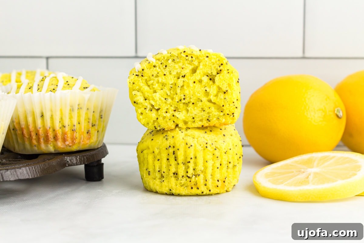 Gluten-free lemon poppy seed muffins stacked to show moist crumb and poppy seeds with fresh lemons in background