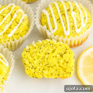 Gluten-free lemon poppy seed muffins with lemon glaze in white liners, one muffin sliced open to show moist crumb and poppy seeds