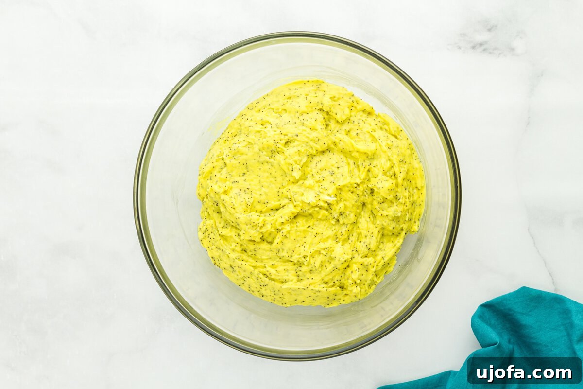 Thick gluten-free lemon poppy seed muffin batter in glass mixing bowl showing bright yellow color and poppy seeds