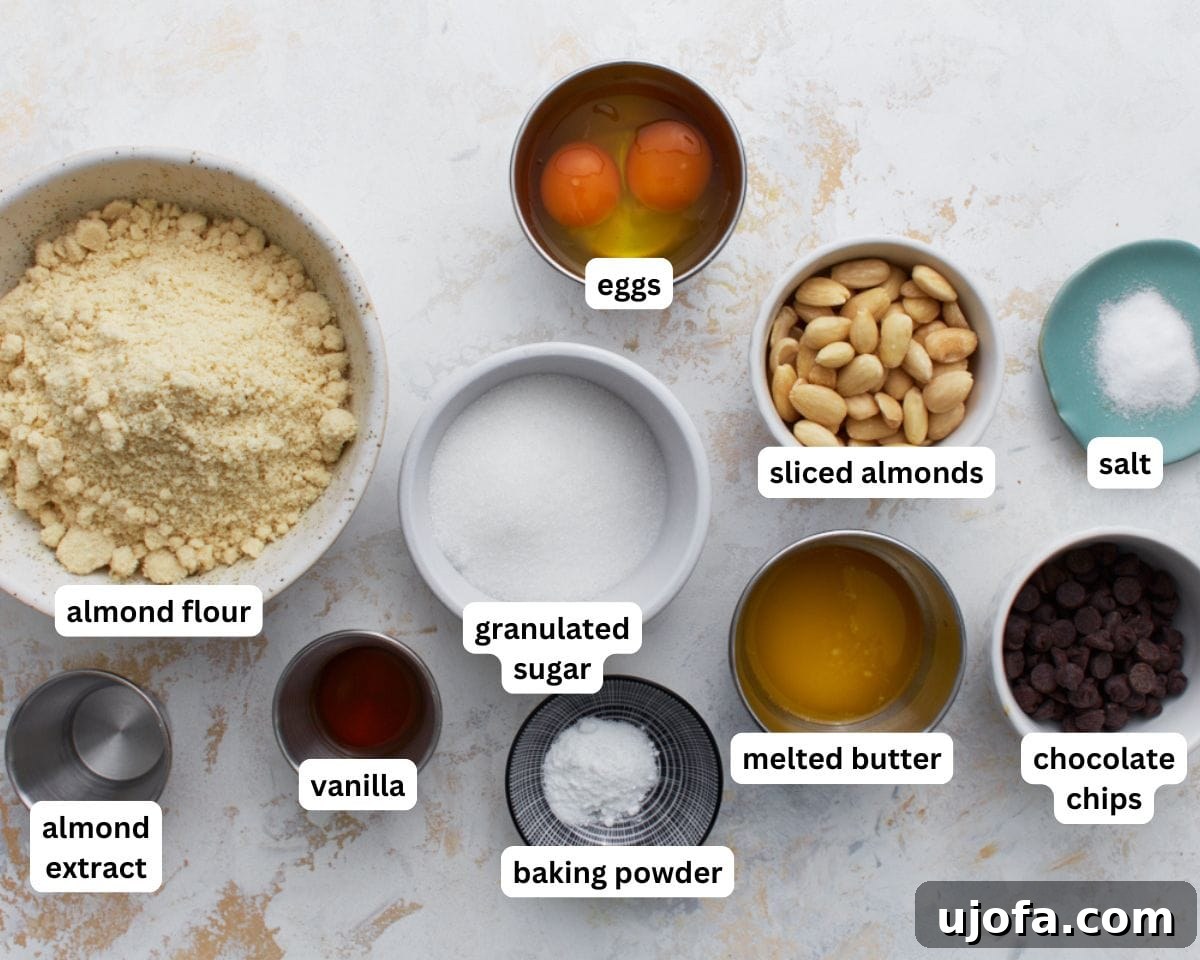 Artisanal Almond Biscotti 3 A collection of ingredients for almond flour biscotti laid out on a white surface, including eggs, butter, extracts, almond flour, sugar, baking powder, salt, sliced almonds, and chocolate chips.