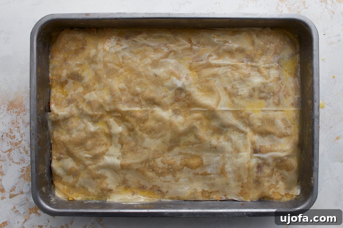 Final layer of butter-brushed gluten-free phyllo dough covering the baklava before baking.