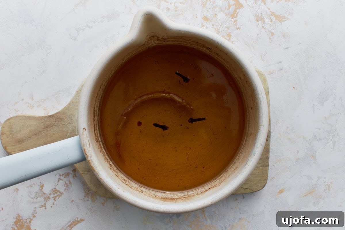 Honey syrup with whole cloves and lemon peel simmering in a small saucepan for gluten-free baklava.
