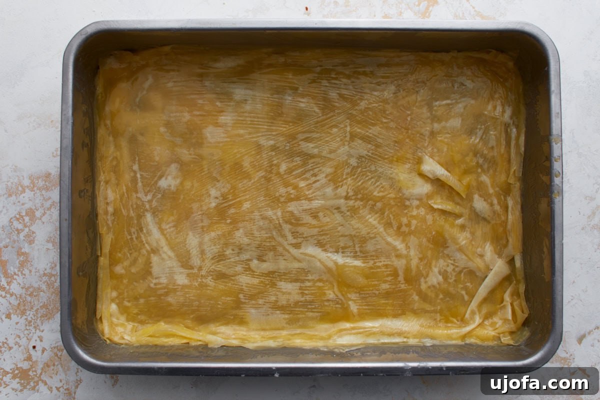 Butter-brushed gluten-free phyllo dough layered in a baking dish for homemade baklava.