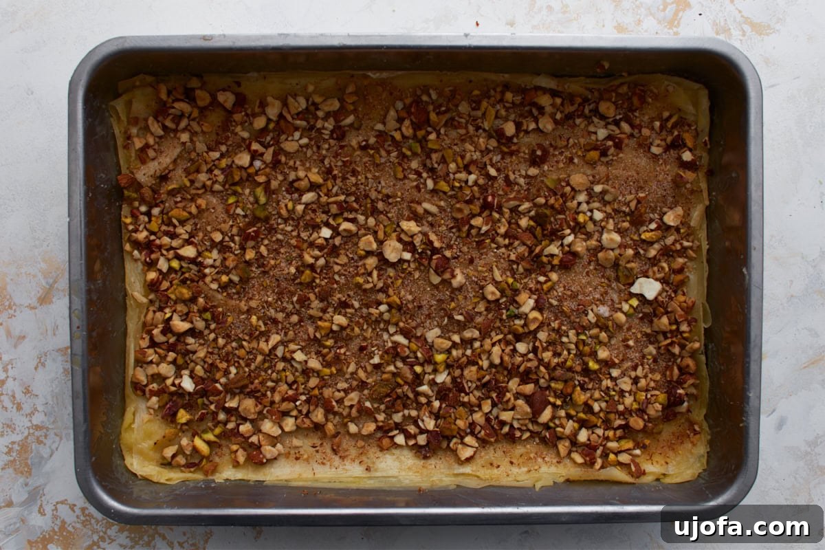 Chopped nut mixture sprinkled over buttered gluten-free phyllo dough in a baking pan.