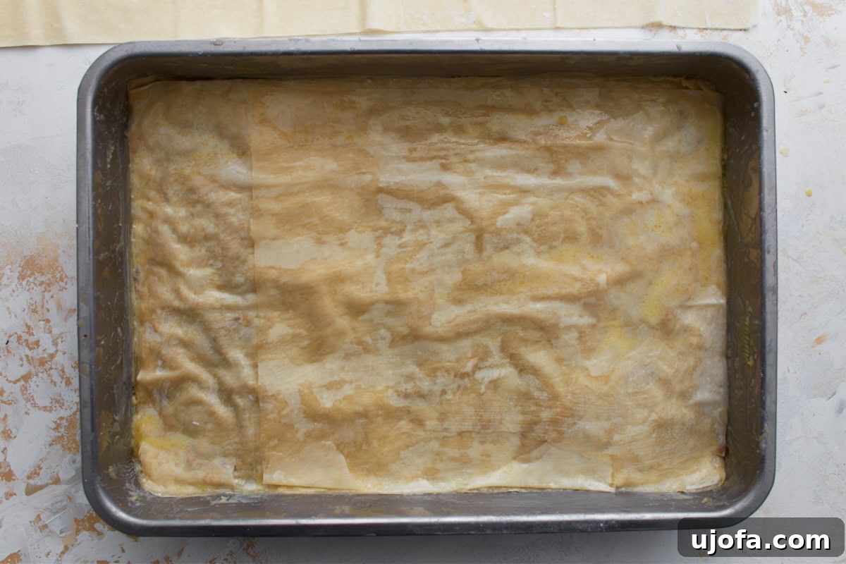 More buttered gluten-free phyllo sheets layered over the nut filling in a baking dish.